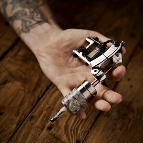 Close up of a man's hand presented new custom made shiny metal tattoo gun